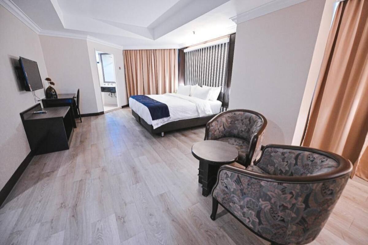 A hotel room with a bed, a desk, a chair, and a small table.