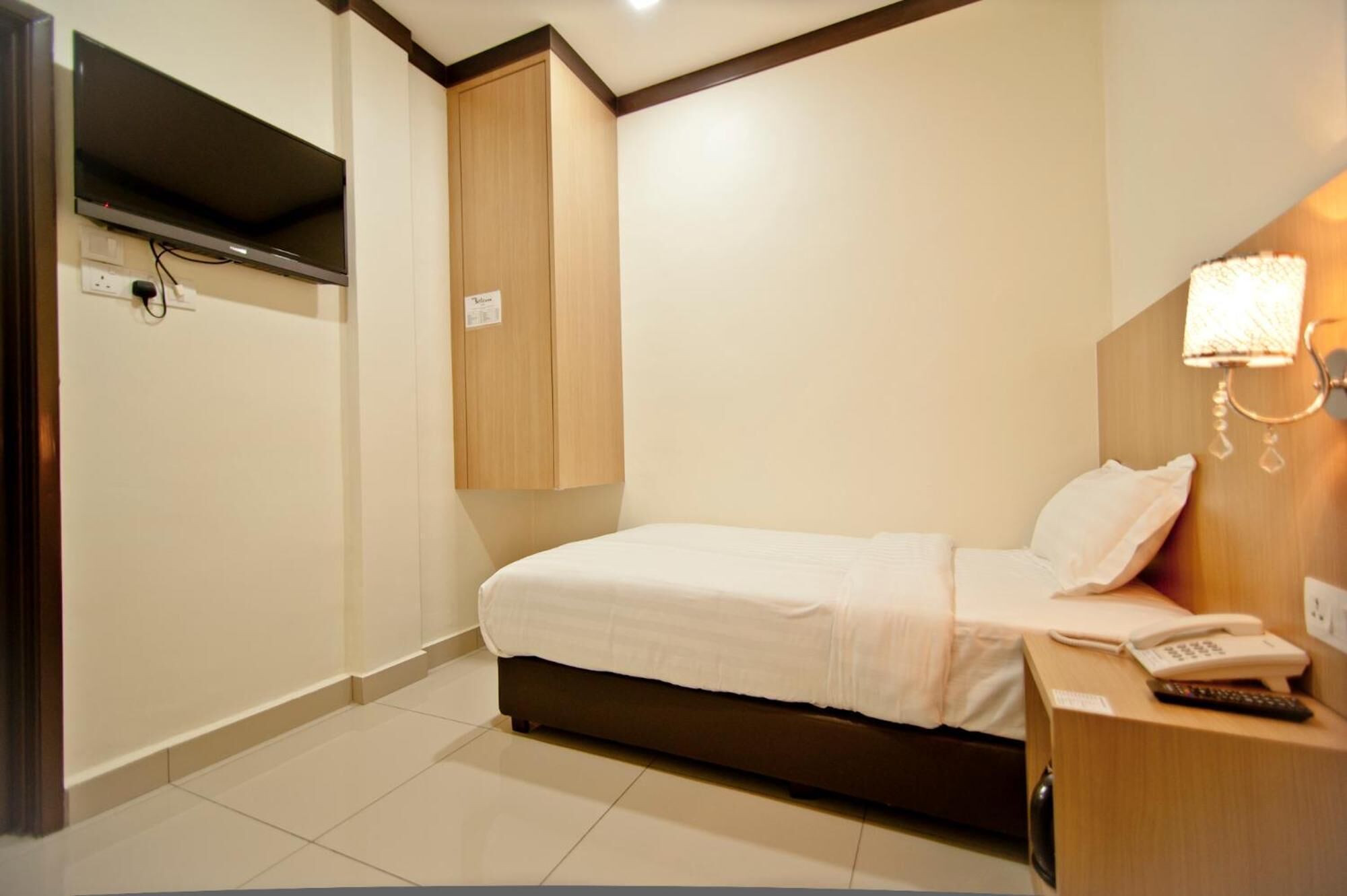 Habitación de hotel con cama, mesita de noche con teléfono y control remoto, televisión montada en la pared y un armario de madera.