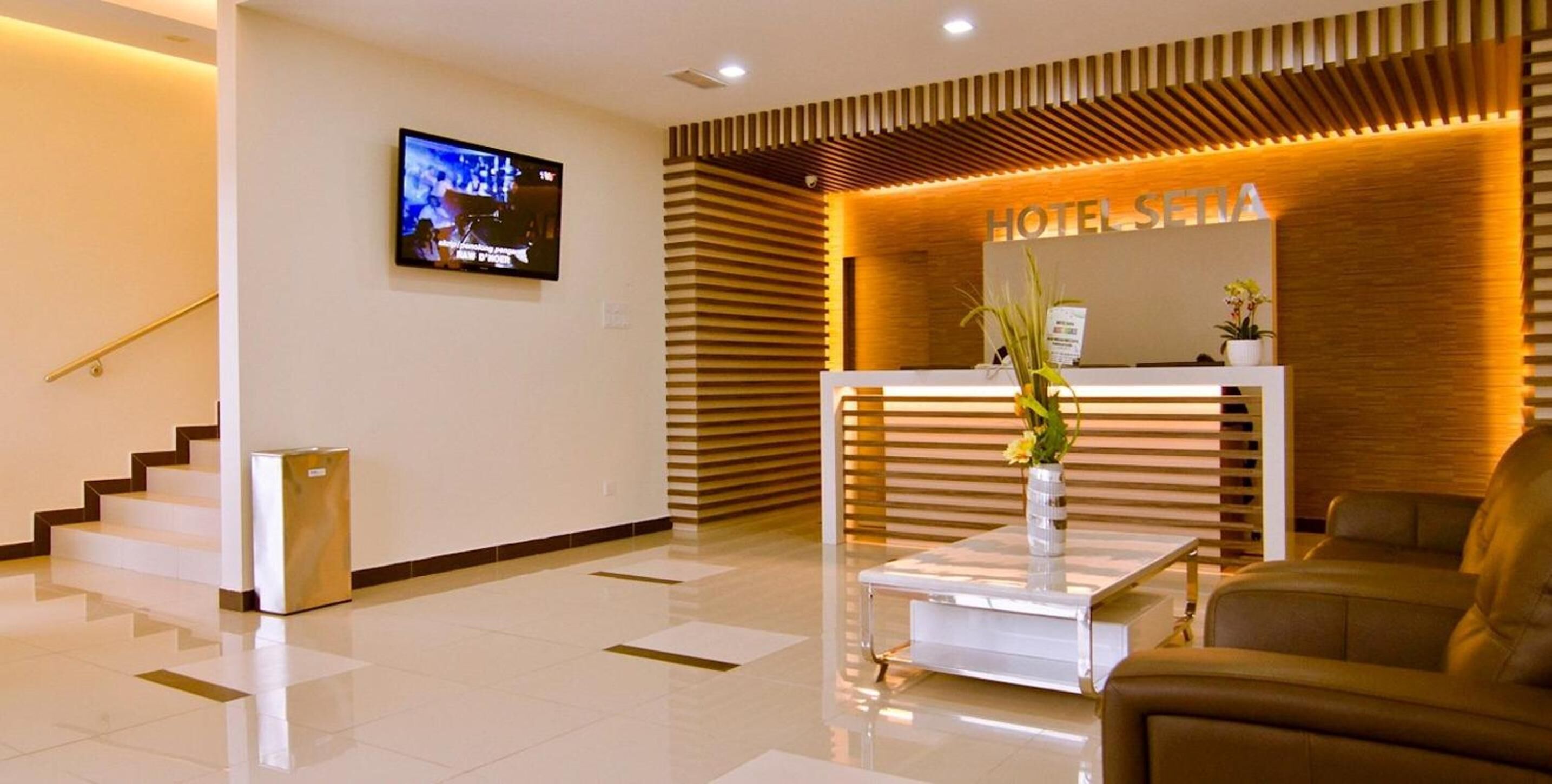 Zona de recepción de un hotel con mostrador, televisor montado en la pared y una escalera que sube a otro piso.