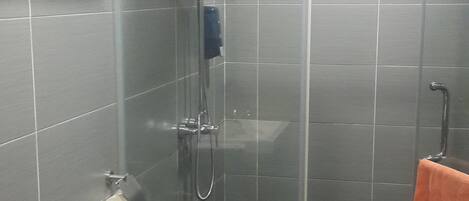 Un baño con inodoro, ducha con mampara de vidrio y un perchero para toallas.