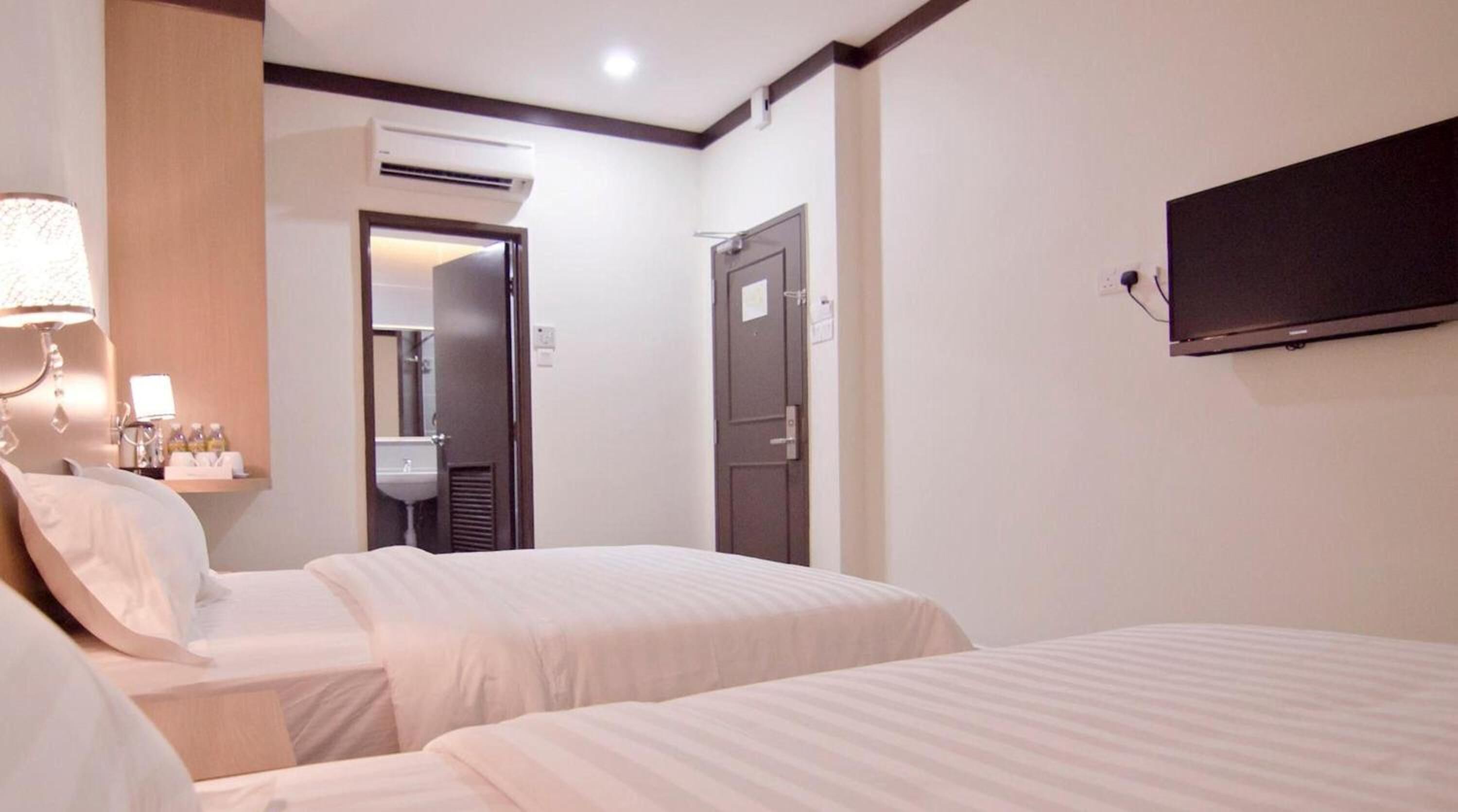 Habitación de hotel con dos camas, un televisor montado en la pared, una lámpara de noche y un aire acondicionado.