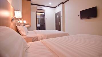 A hotel room with two beds, a wall-mounted TV, and a bathroom visible through an open door.