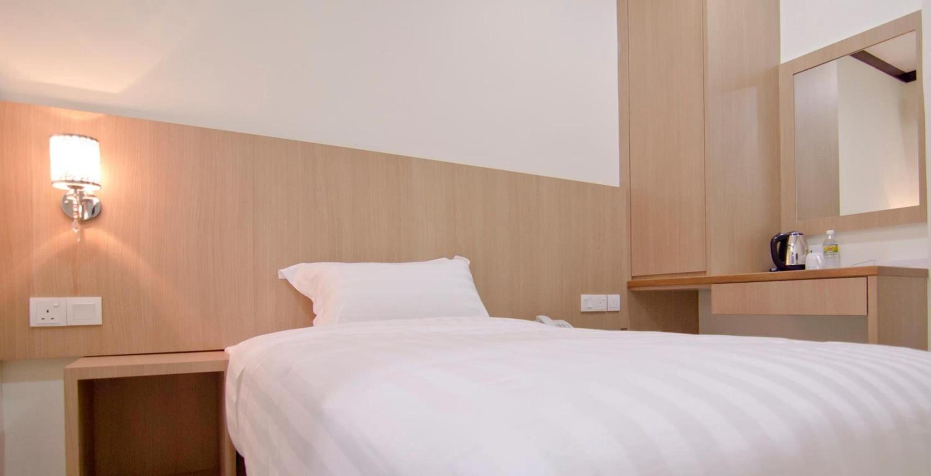 Et hotelværelse med en seng, et natbord, en væglampe, et spejl og en hylde med toiletartikler.