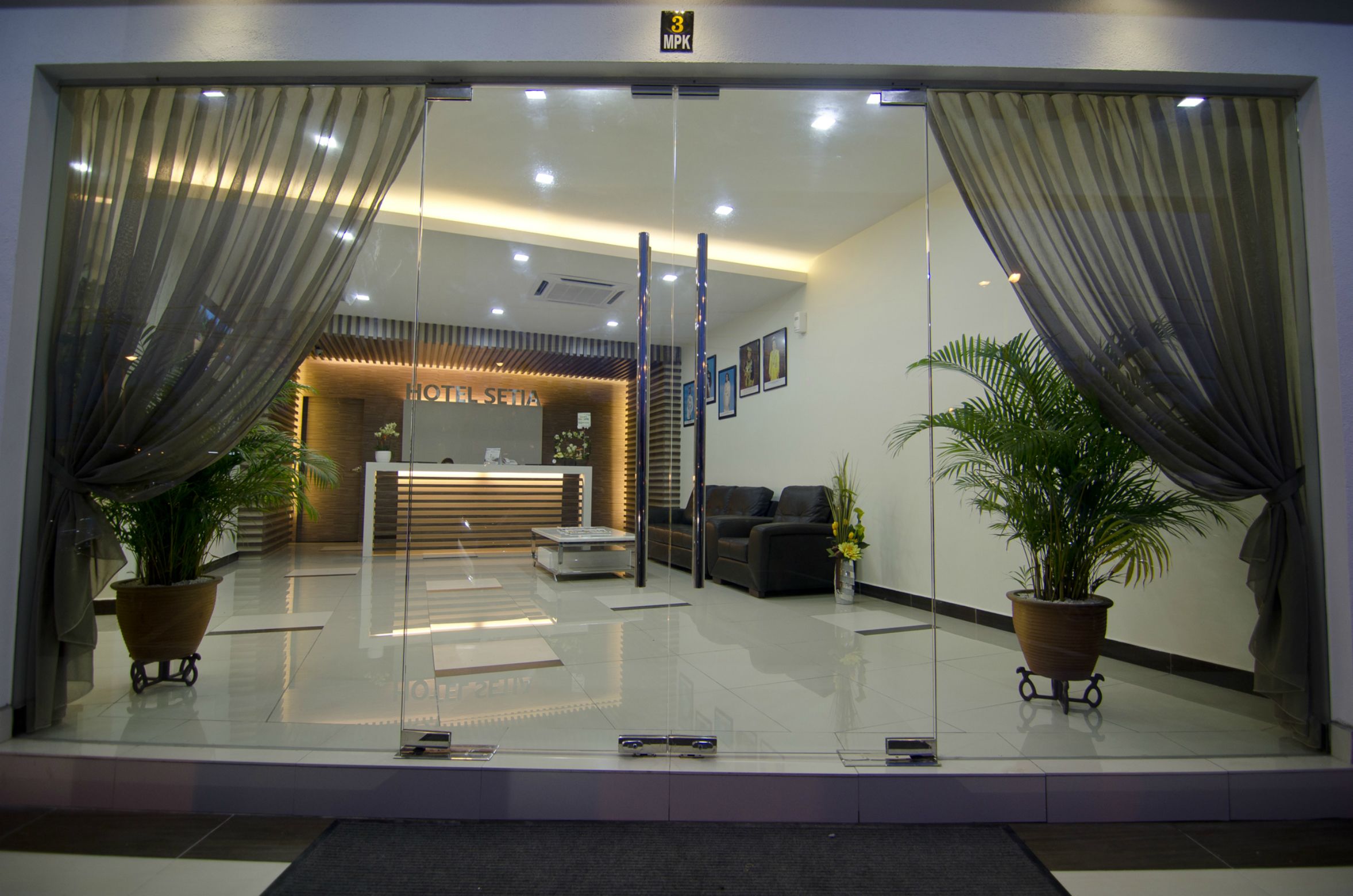 A hotel reception area with a modern design, featuring a reception desk, seating area, and potted plants.