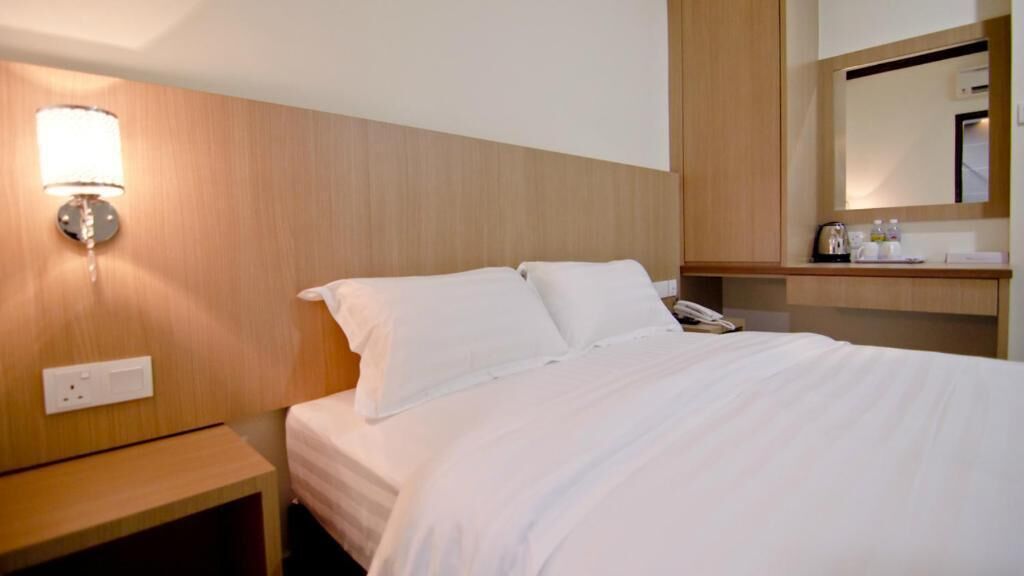 Una habitació d'hotel amb llit, taulella de nit, làmpada i un mirall sobre la taulella.