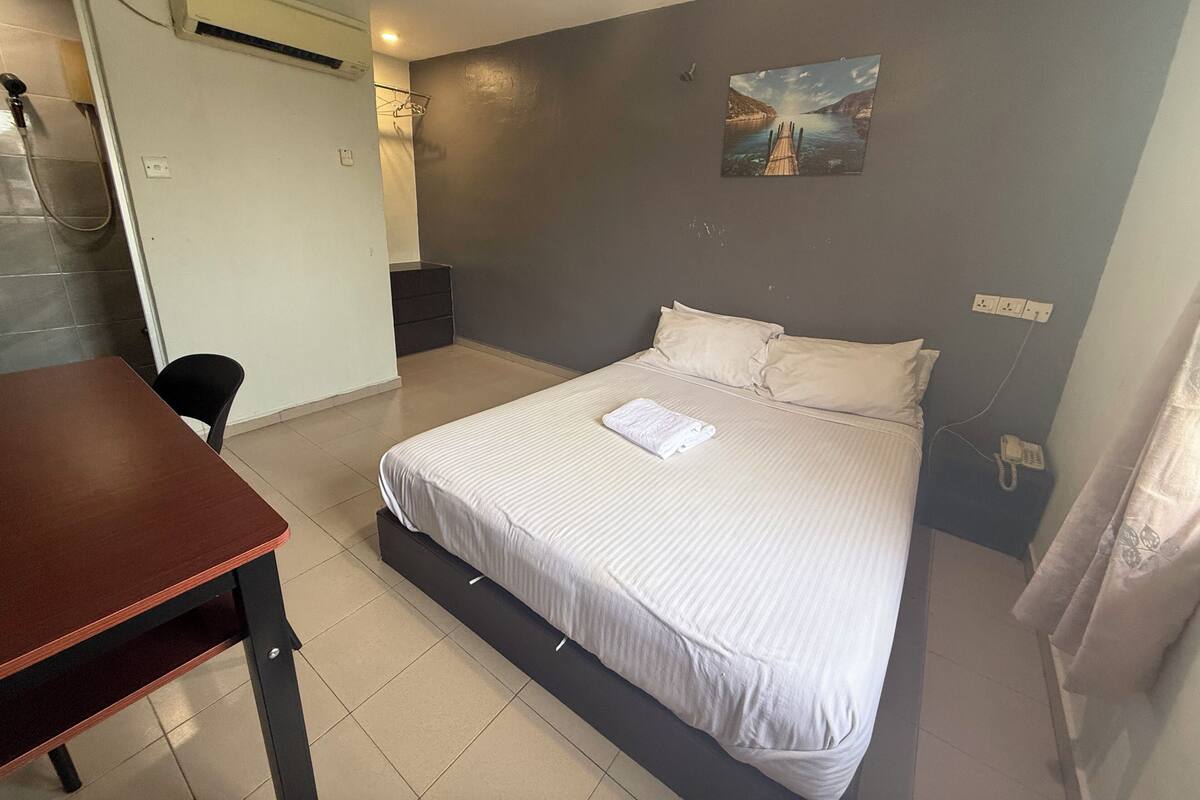 Une chambre à coucher avec un lit, un bureau, une chaise, un tableau accroché au mur et une porte de salle de bain.