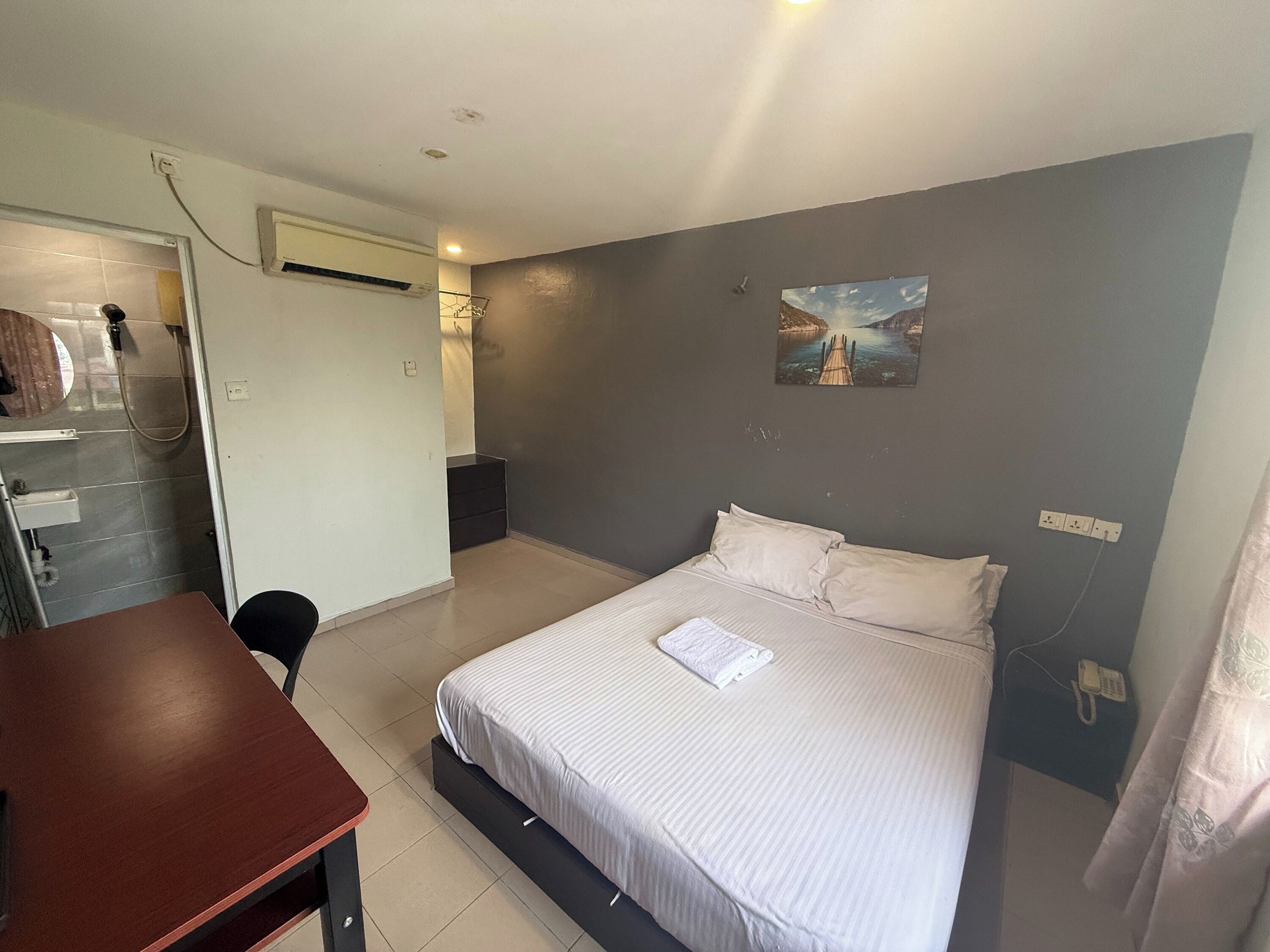 A bedroom with a bed, a desk, a shower, and a painting on the wall.