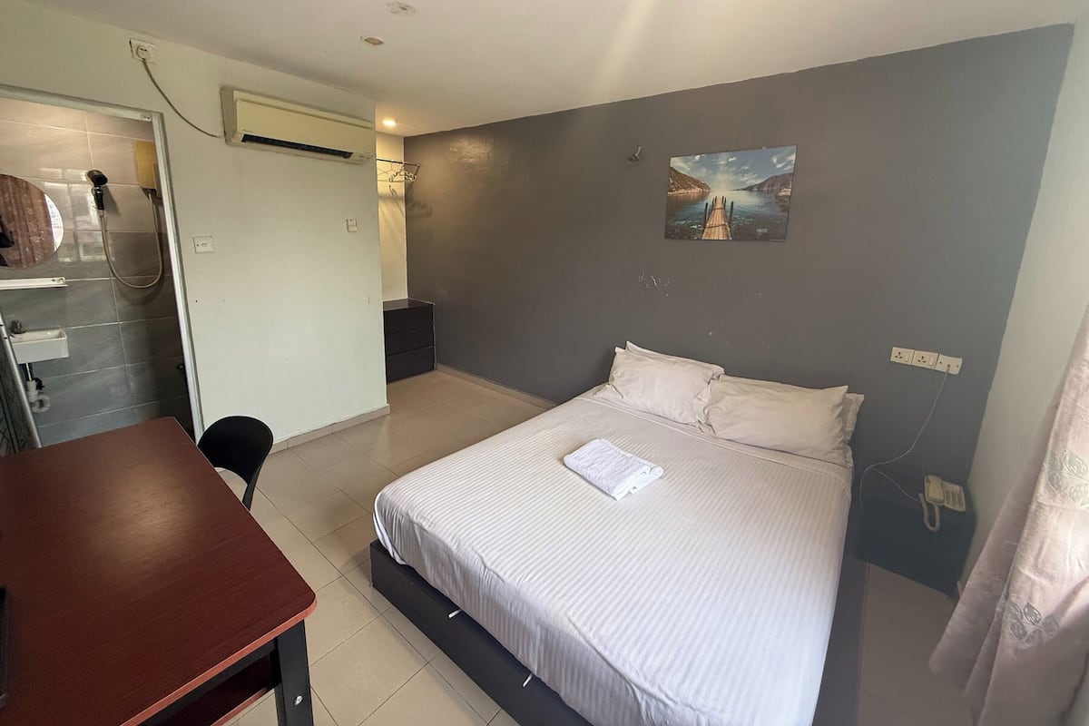 A bedroom with a bed, a desk, a shower, and a painting on the wall.