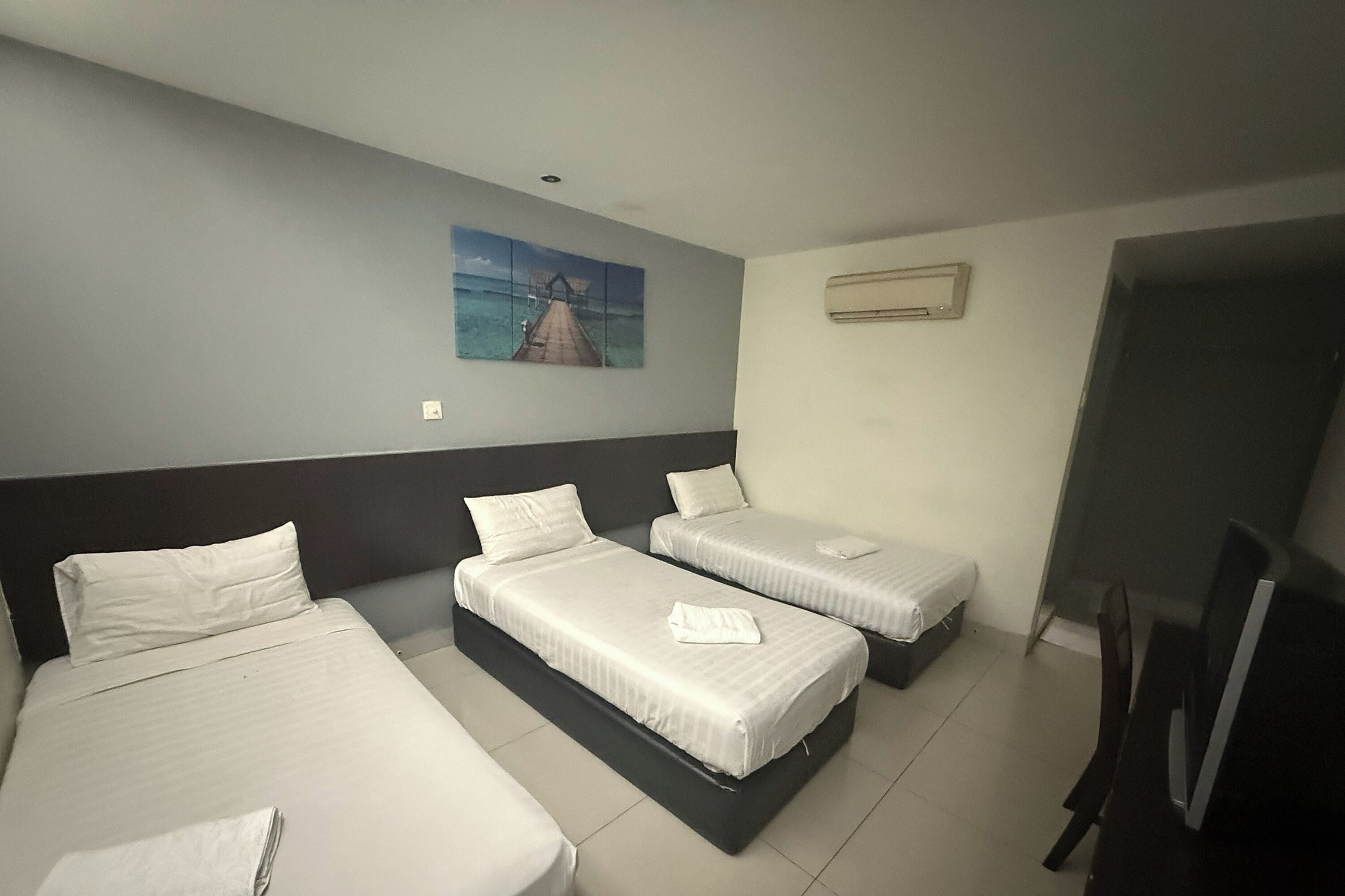 Quarto de hotel com três camas, um quadro na parede, aparelho de ar condicionado e televisão.