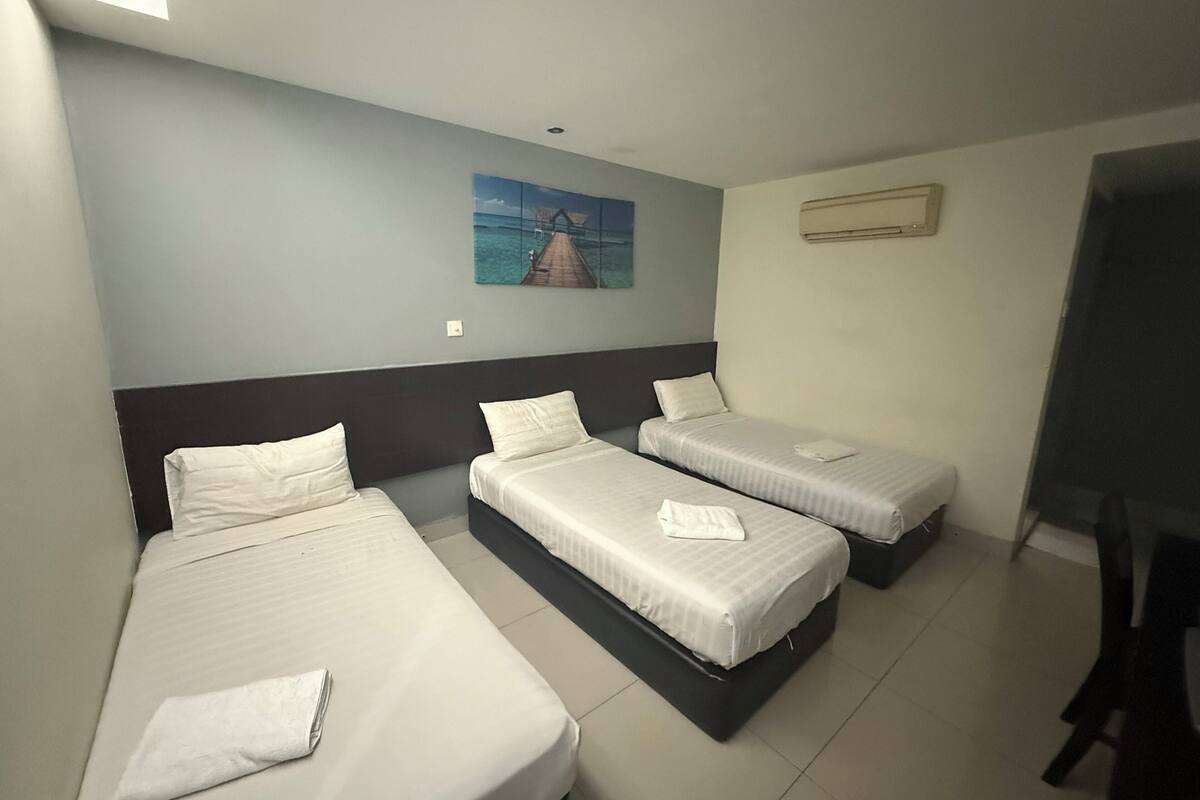 Une chambre d’hôtel avec trois lits simples, un tableau au mur et un téléviseur sur le côté droit.
