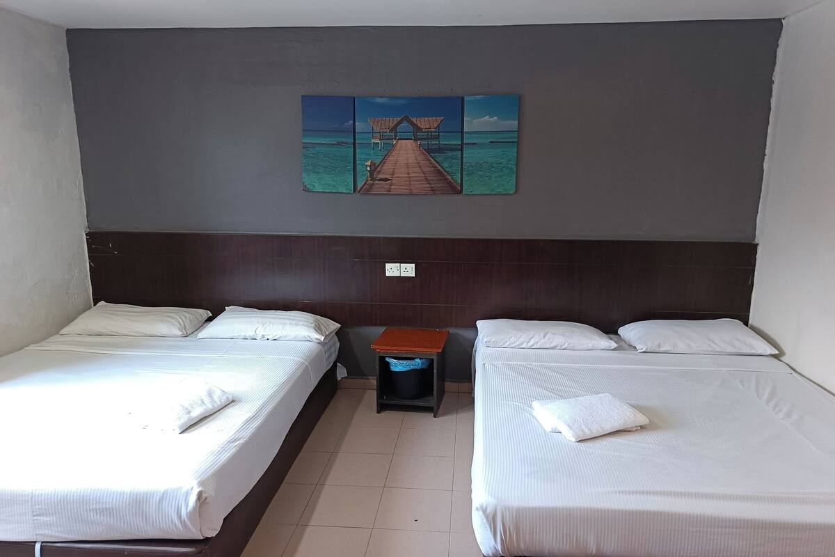 Une chambre d’hôtel avec deux lits, une petite table et un tableau accroch é au mur représentant une jetée.