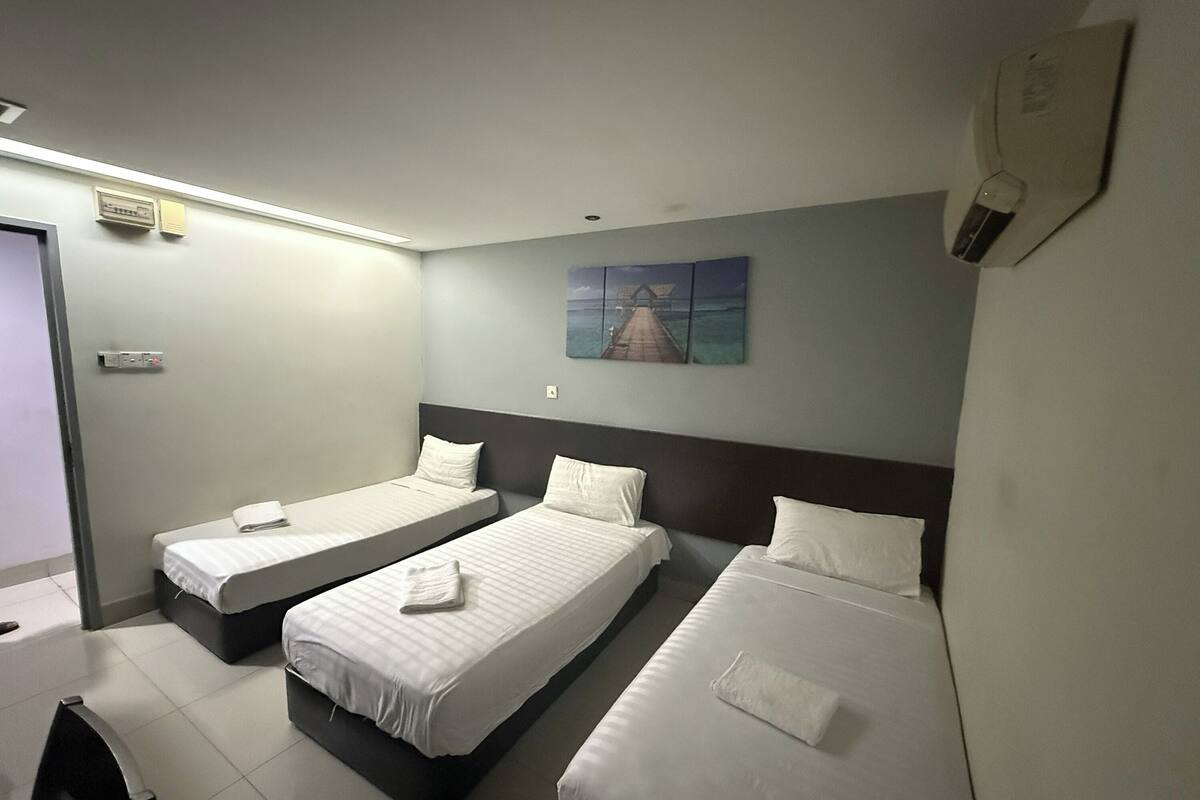 Une chambre d’hôtel avec trois lits simples, un tableau au mur et un ventilateur de plafond.
