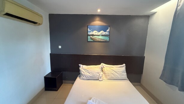 A hotel room with a bed, a nightstand, a wall-mounted air conditioner, and a painting of a beach scene. - Tiong Nam Hotel Near Pasir Gudang (Pasir Gudang)