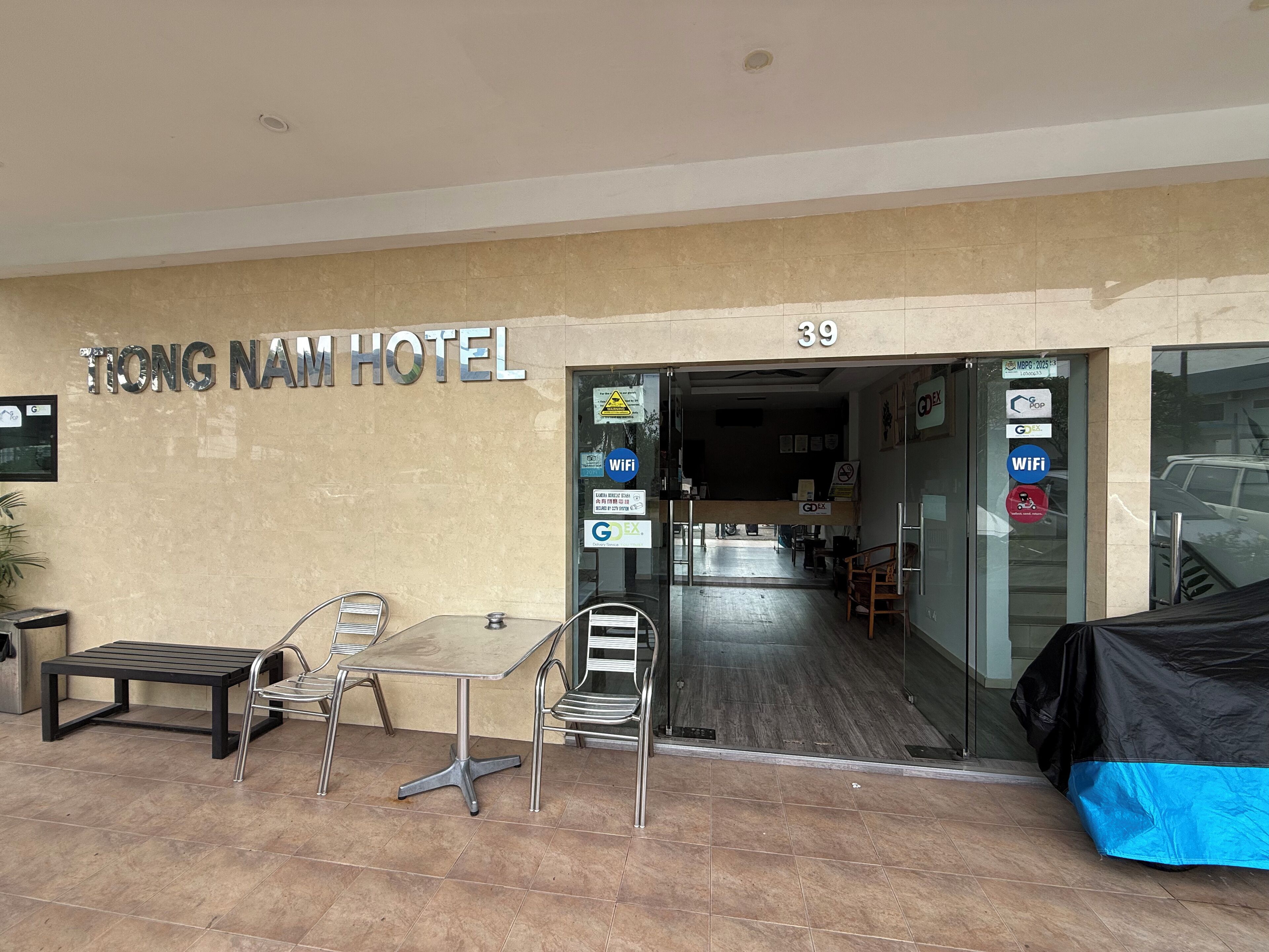 The entrance to Tong Nam Hotel with a reception desk, a waiting area with chairs and a table, and a sign indicating the hotel's name and room number.