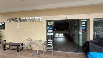 The entrance to Tong Nam Hotel with a reception desk, a waiting area with chairs and a table, and a sign indicating the hotel's name and room number.