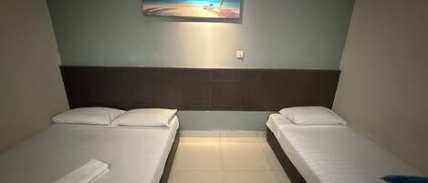 Habitación de hotel con dos camas individuales, una mesita de noche, un cuadro de una escena de playa y suelo de baldosas.
