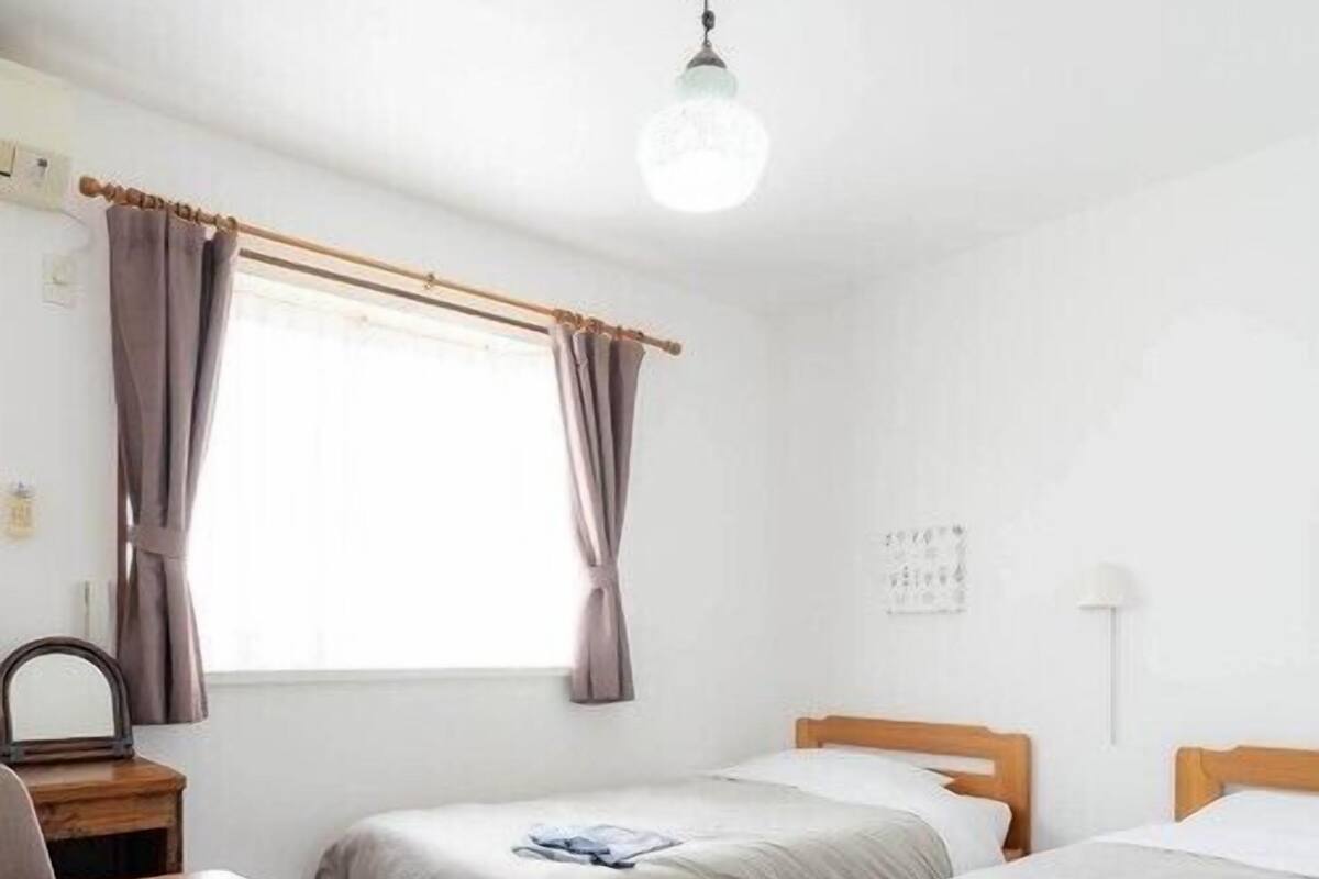 Une chambre avec deux lits, un bureau, une chaise et une fenêtre avec des rideaux.