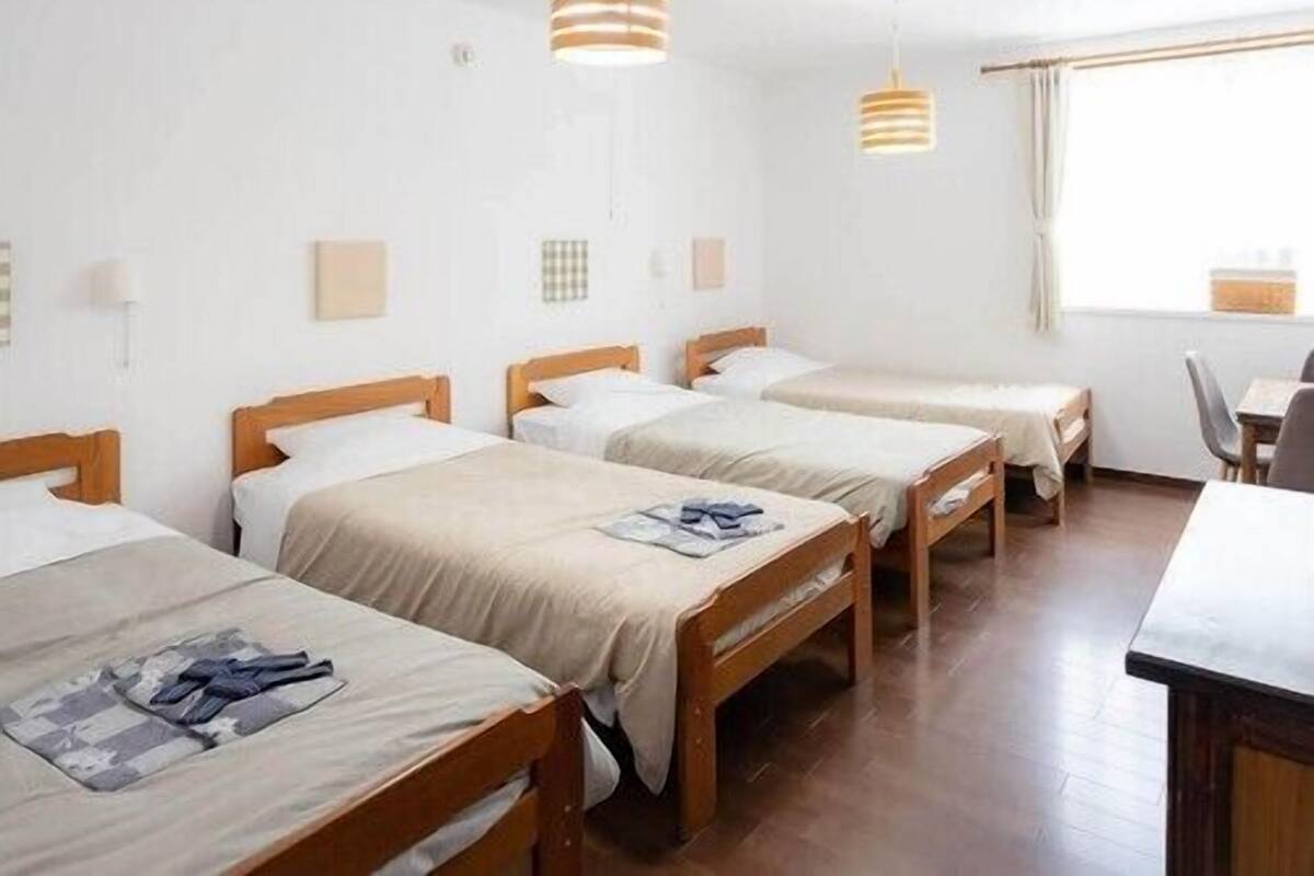 Une chambre d’hôtel avec trois lits en bois, un bureau et deux lampes suspendues.