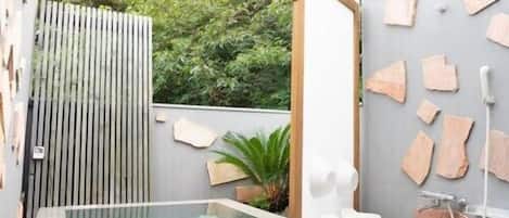 A modern bathroom with a glass-enclosed hot tub, a wooden slatted wall, and a stone-tiled floor.