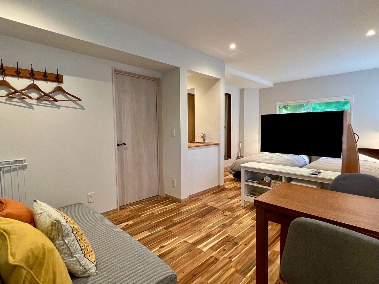 Una habitación de hotel pequeña con cama, escritorio, silla, televisión y perchero.