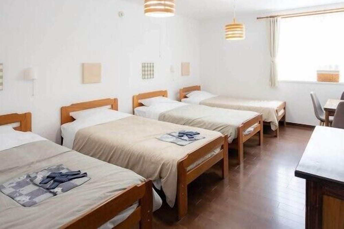 Une chambre d’hôtel avec trois lits en bois, un bureau en bois et une fenêtre avec des rideaux.