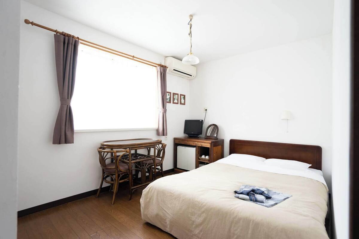 Une chambre à coucher comprenant un lit, un bureau avec une chaise, un climatiseur, un téléviseur et une lampe fixée au mur.
