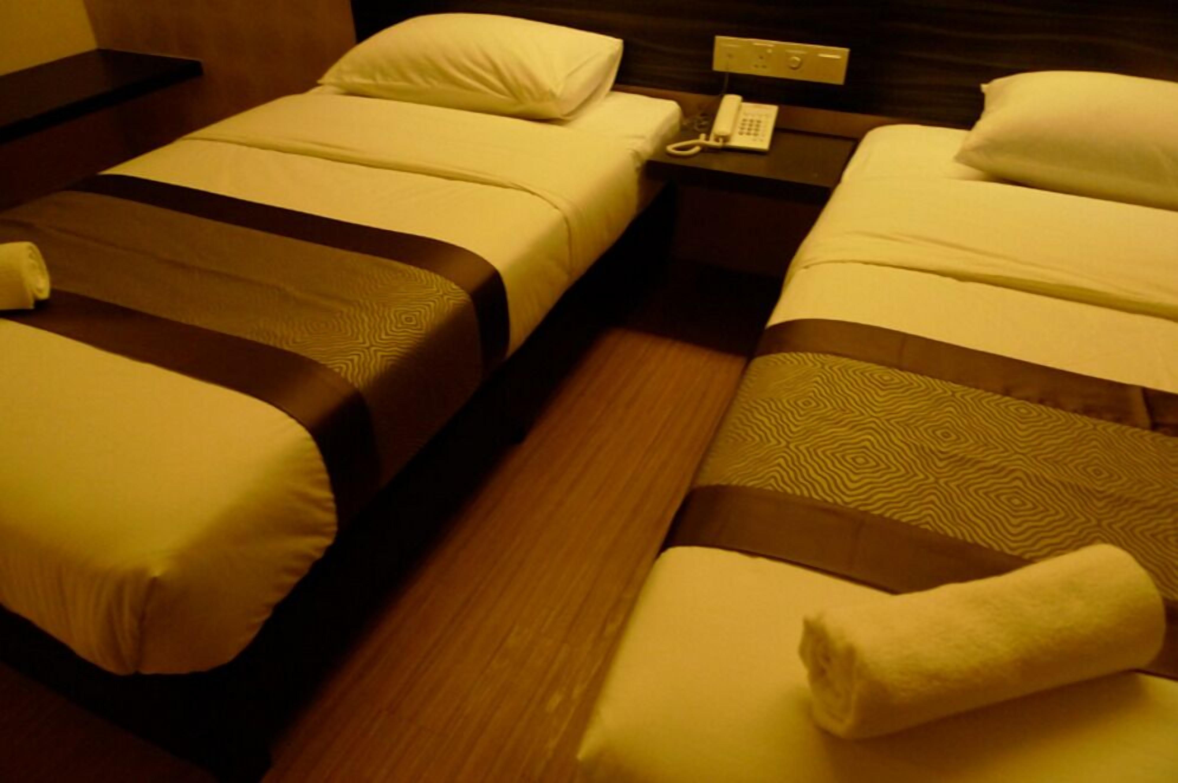 A hotel room with two beds, each with a white pillow and a brown headboard. There is a telephone on the nightstand between the beds.