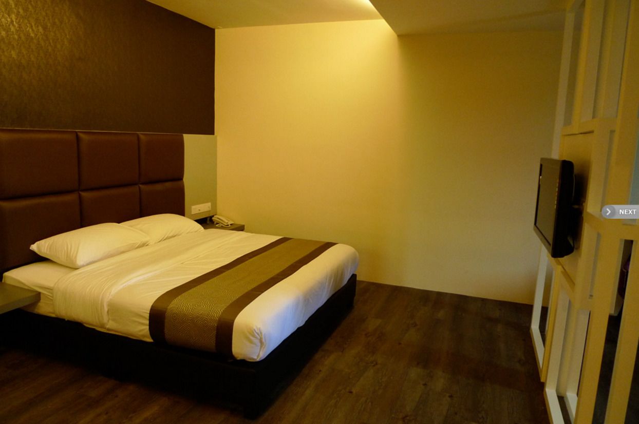 Habitación de hotel con cama, mesita de noche, televisor y piso de madera.