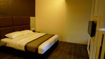 Habitación de hotel con cama, mesita de noche, televisor y piso de madera.