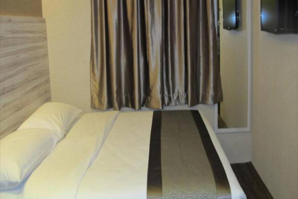 Een hotelkamer met een bed, gordijnen en een flatscreen televisie aan de muur.