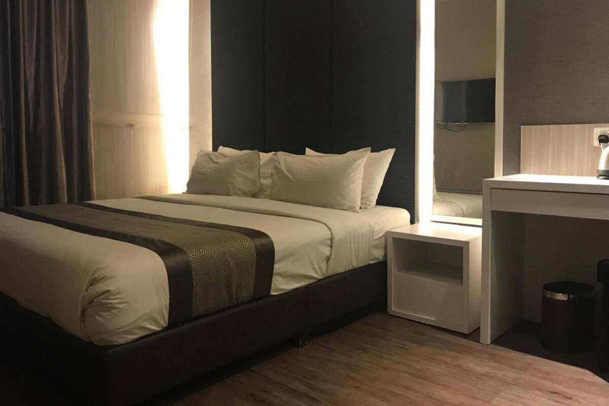 Een moderne hotelkamer met een groot bed, nachtkastjes, een spiegel en een kleine prullenbak.
