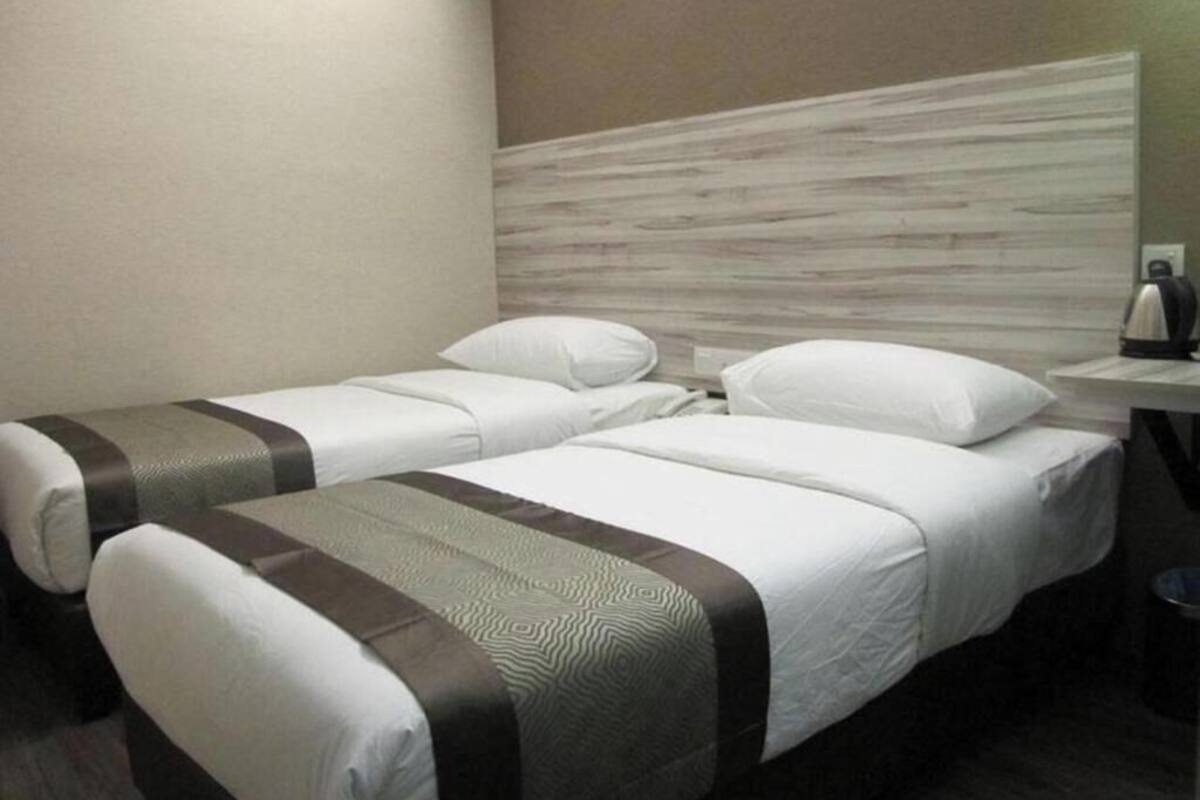 Een hotelkamer met twee enkele bedden, een houten hoofdeinde, een nachtkastje met een lamp en een prullenbak.