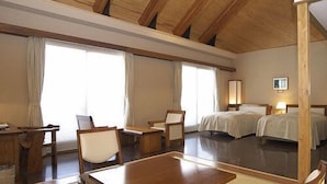 Une chambre d’hôtel avec un plafond en bois, un coin repas avec une table et des chaises, deux lits et un téléviseur.
