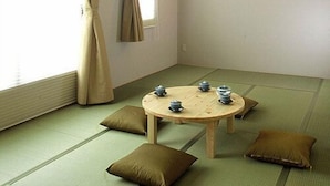 Une pièce avec un sol recouvert de tatamis, comprenant une table ronde, des coussins et un luminaire fixé au mur.