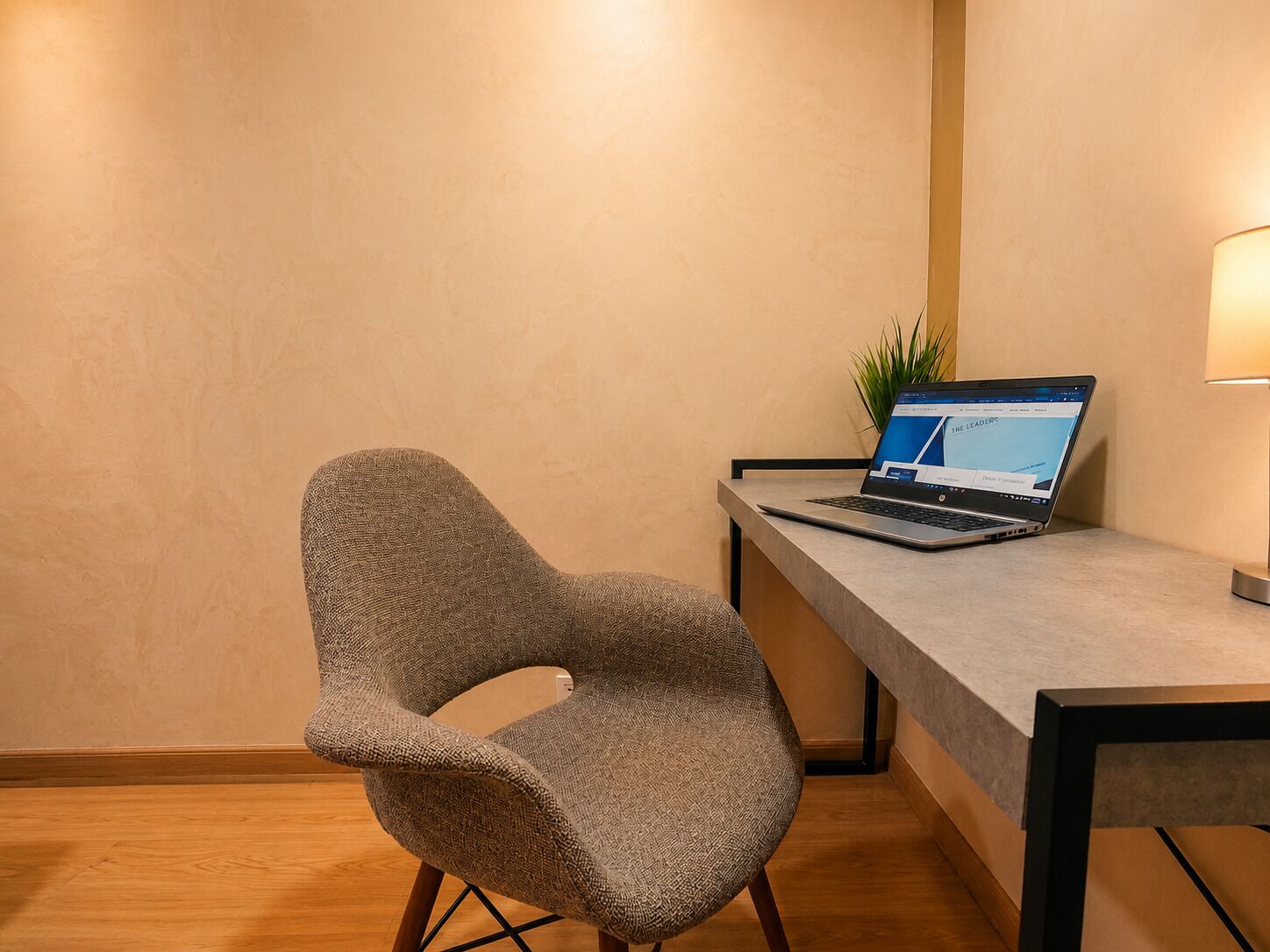 A modern room with a curved chair, a desk with a laptop, and a lamp.