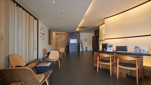 Un moderno hall de hotel con mostrador de recepción, zona de estar y una gran pared con un reloj.