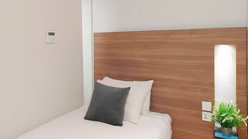 A hotel room with a wooden headboard, a bed with white bedding and two pillows, a small potted plant on the nightstand, and a wall-mounted air conditioning unit.