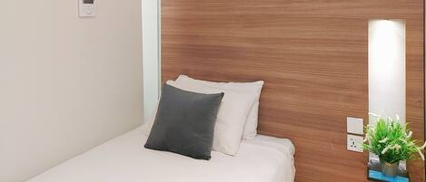 A hotel room with a wooden headboard, a bed with white bedding and two pillows, a small potted plant on the nightstand, and a wall-mounted air conditioning unit.