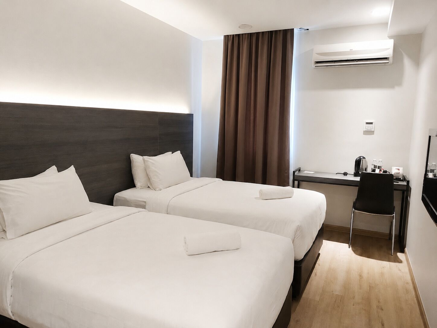 A hotel room with two beds, a desk, a chair, an air conditioning unit, and a mirror.