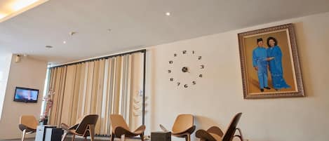 Un vestíbulo amplio con sillas modernas, un reloj grande y un retrato enmarcado en la pared.