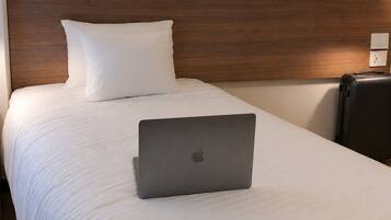Una cama bien hecha con ropa blanca, una laptop en la cama y una maleta en el suelo.