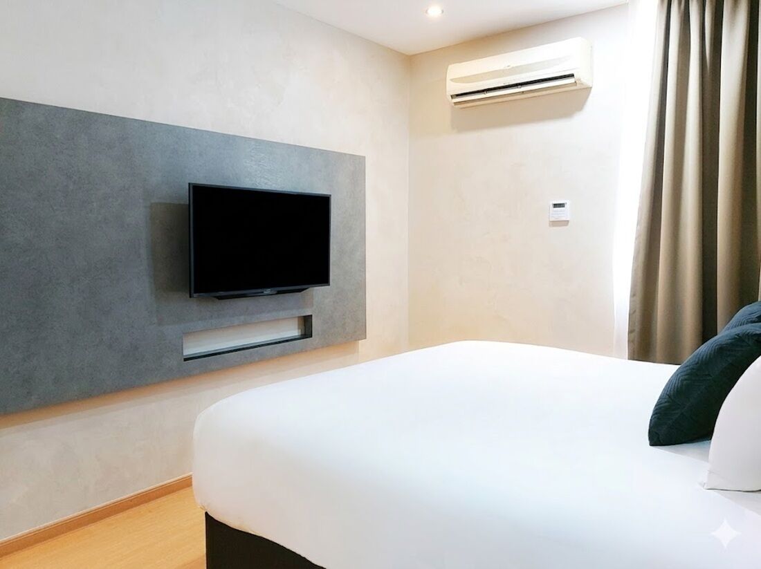 Una camera d'albergo moderna con una TV a schermo piatto montata su una parete grigia, un letto con biancheria bianca e un condizionatore d'aria a parete.
