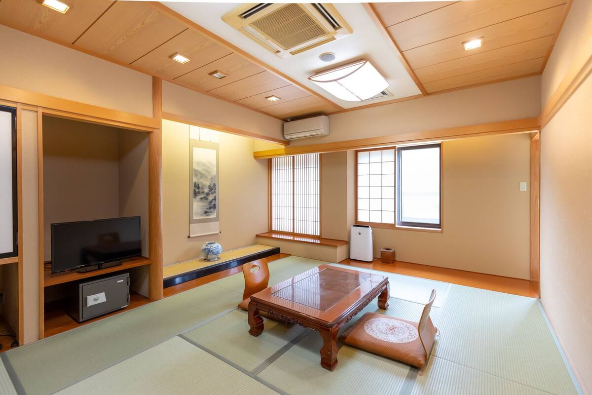 Una habitación de estilo japonés tradicional con suelo de tatami, una mesa de madera baja, un televisor y puertas correderas.