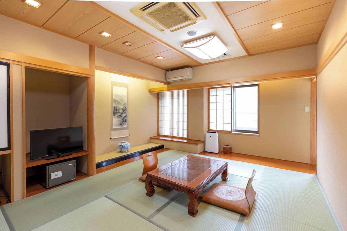 Una habitación tradicional japonesa con suelo de tatami, una mesa baja, un televisor y puertas correderas.