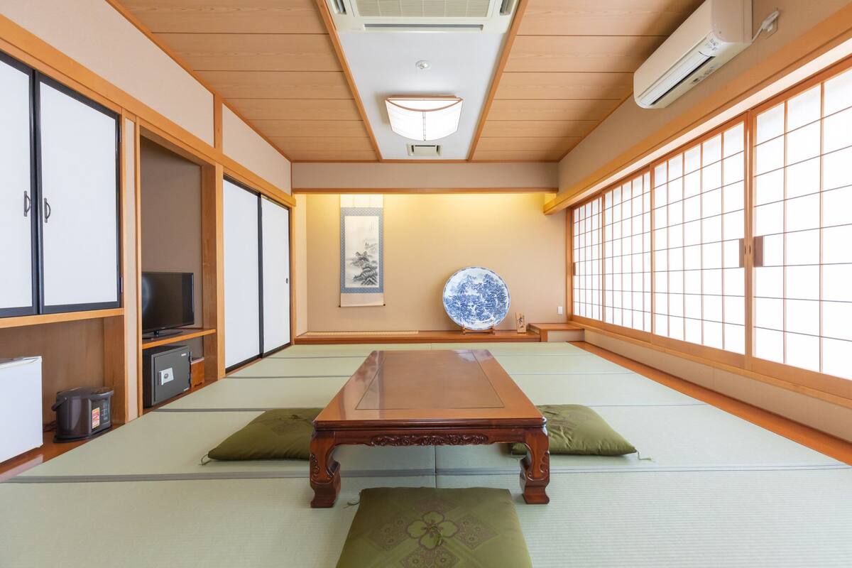 Una habitación japonesa tradicional con suelo de tatami, una mesa de madera baja, puertas correderas y un ventanal con diseño de cuadrícula.