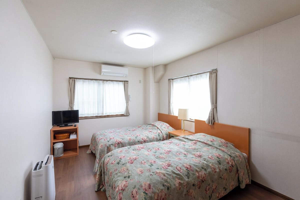 Una habitación de hotel pequeña con dos camas, un televisor, una lámpara y un calentador.