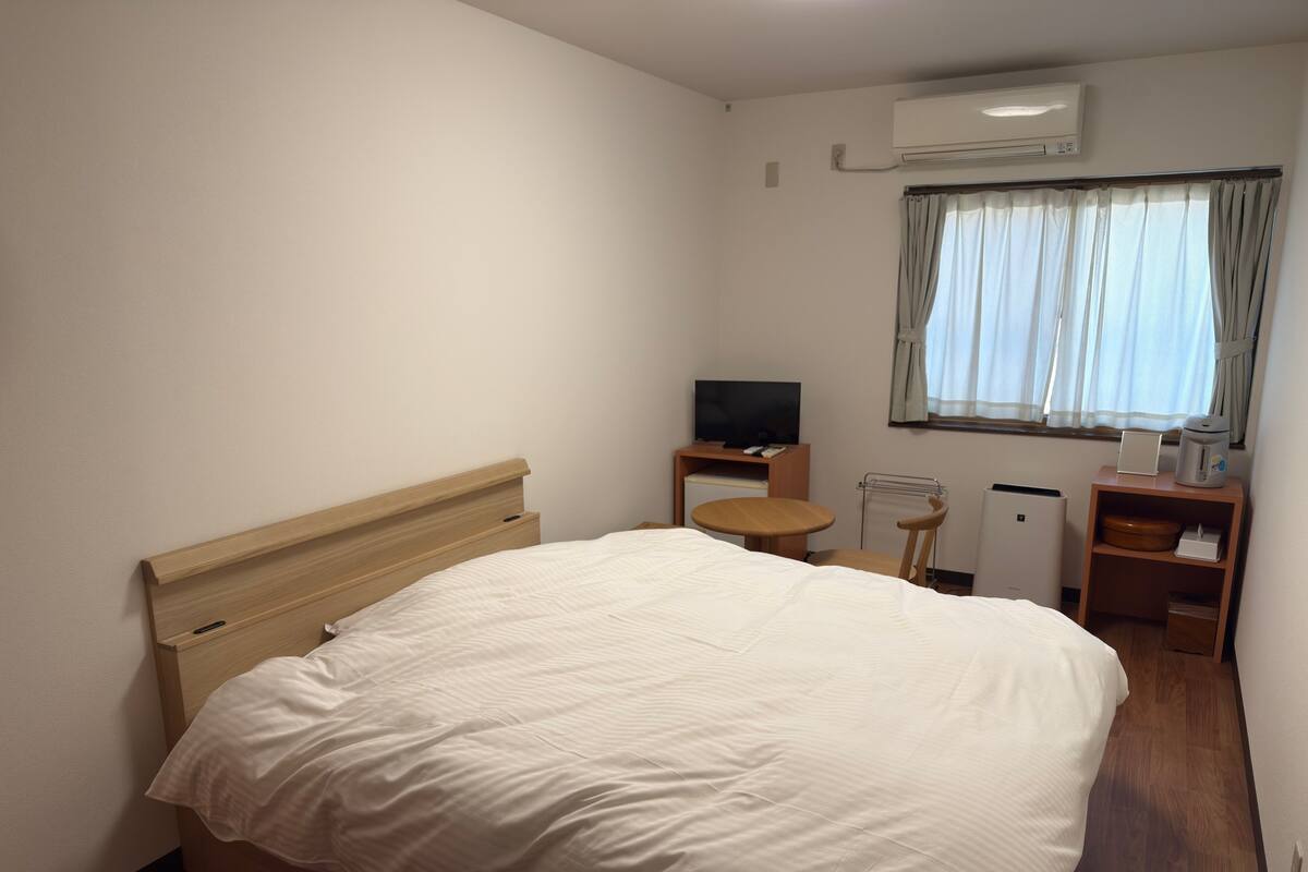 Habitación de hotel con cama, televisor, cafetera y ventana con cortinas.