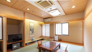 Habitació japonesa tradicional amb fons de tatami, una taula de fusta baixa, una televisió i portes corredisses.