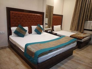 A hotel room with a large bed, a bedside table, a nightstand, a mirror, and a window with curtains. - Indo Continental (Delhi)