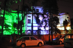 A building with illuminated green and blue lights, parked cars, and palm trees.